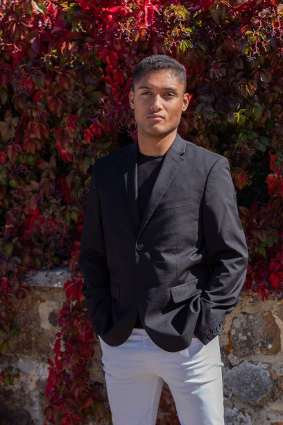 一个穿着黑色夹克和白色裤子的年轻男子的肖像，双手插在裤子口袋里图片下载