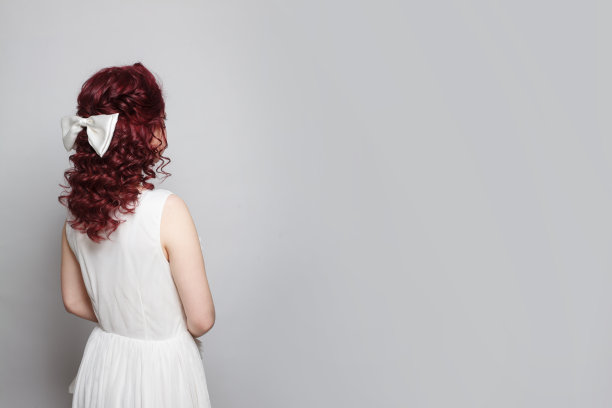 美丽的女人，红色卷发，白色连衣裙，蝴蝶结，站在她的背后图片下载