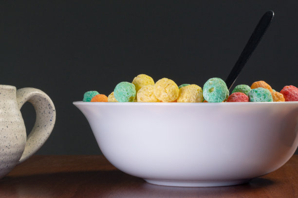 木桌上有一个小杯子，旁边放着一碗五颜六色的含糖麦片图片下载