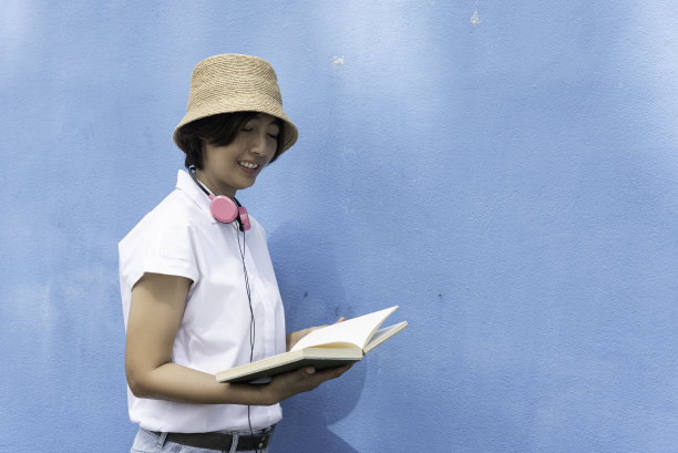 女人看书放松后，手里拿着书，戴着耳机听音乐。图片下载