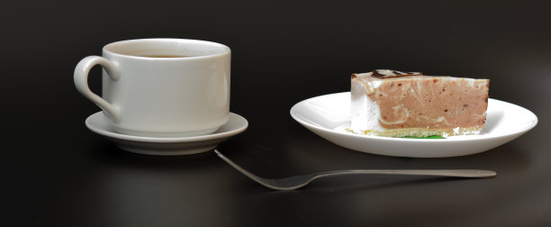 一杯热黑咖啡放在碟子上，一把叉子和一个盘子，黑色背景上有一块新鲜的芝士蛋糕。图片下载