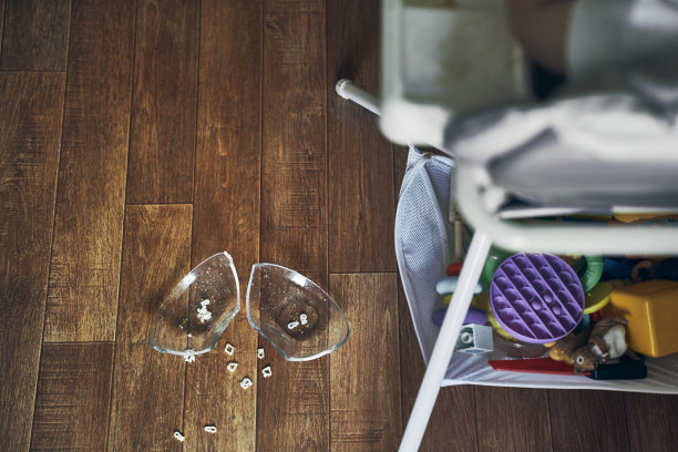 一个坐在高脚椅上的小婴儿把一杯汤面掉在了木地板上。透明板分为两部分。面条在图形的形式。桌子是脏的。高质量照片图片下载