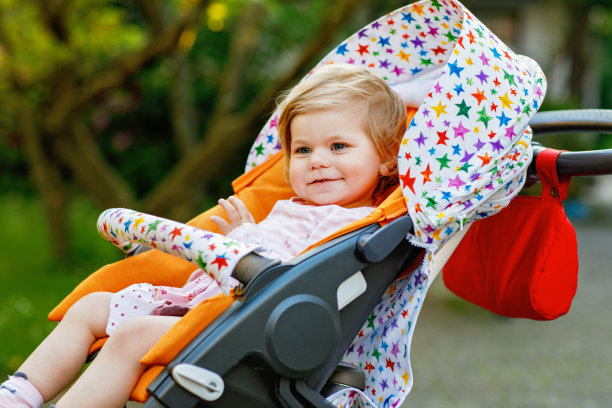 小可爱的微笑蹒跚学步的女孩坐在婴儿车或婴儿车的肖像，去散步。快乐可爱的宝宝在户外玩得很开心。健康的女儿。图片下载