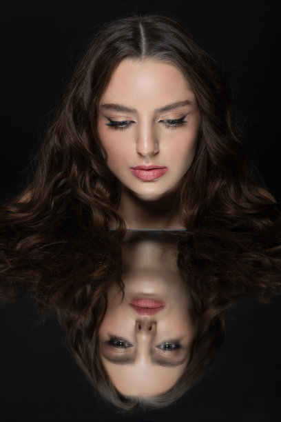 美丽的女人的肖像与波浪的头发和脸反射在镜子图片下载