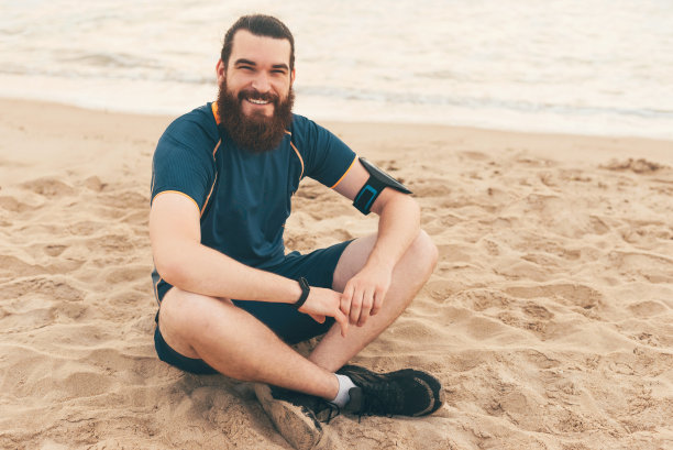 照片中的微笑大胡子男子，坐在沙滩上，放松后的晨练图片下载