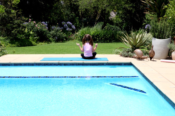 夏天，年轻的女孩在花园里做瑜伽，在一个蓝色的运动垫上，穿着粉红色的上衣，坐下来图片下载