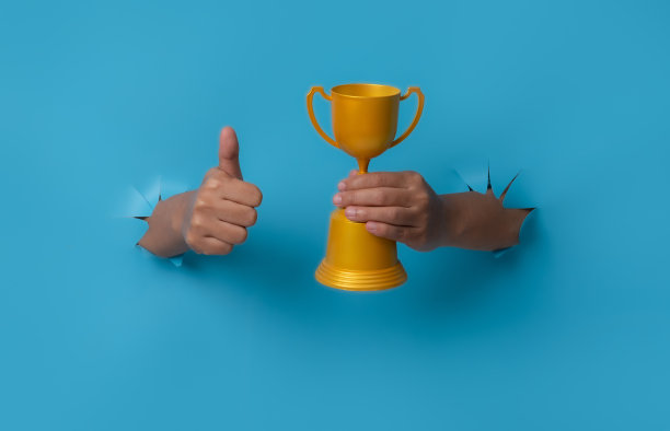 手持冠军金杯的女性手从蓝色的纸背景中突破。图片下载