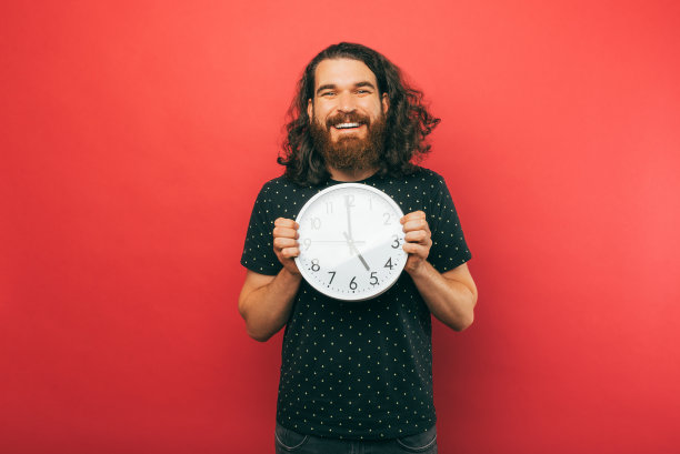 年轻英俊的男子拿着一个圆形的白色时钟，微笑着对着镜头。图片下载