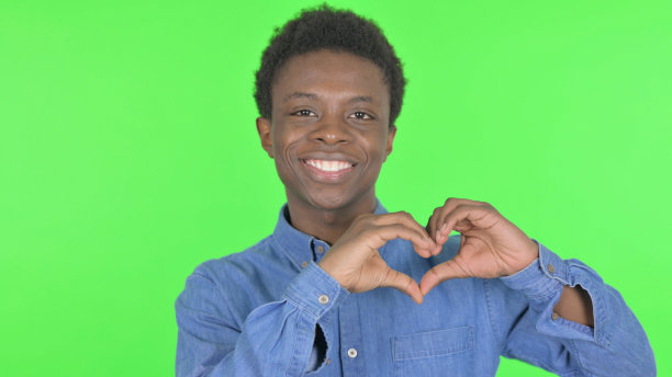 年轻的非洲男子在绿色背景下展示爱的心图片下载