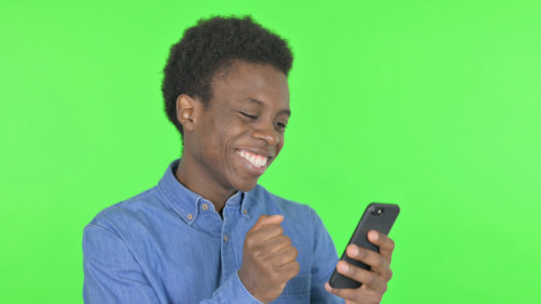 年轻的非洲男子在绿色背景的智能手机上庆祝图片下载