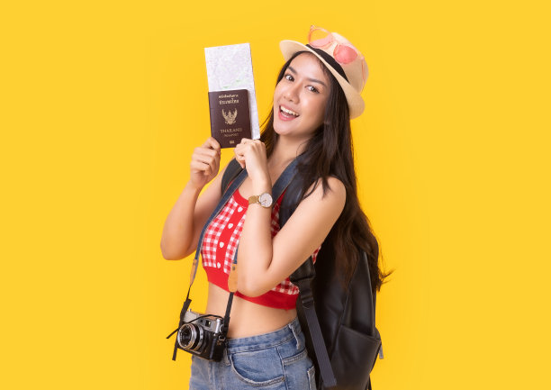 年轻的亚洲女性带着复古相机，黄色背景的护照或带着行李箱和护照度假。微笑快乐的女人手使用智能手机信用卡。图片下载