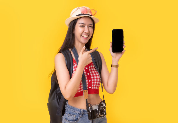 年轻的亚洲女性带着复古相机，黄色背景的护照或带着行李箱和护照度假。微笑快乐的女人手使用智能手机信用卡。图片下载
