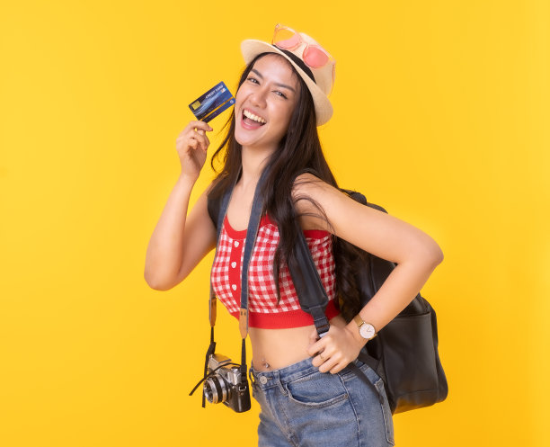 年轻的亚洲女性带着复古相机，黄色背景的护照或带着行李箱和护照度假。微笑快乐的女人手使用智能手机信用卡。图片下载