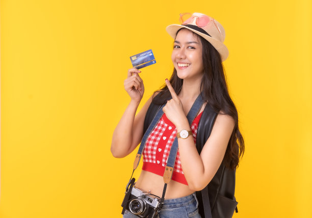 年轻的亚洲女性带着复古相机，黄色背景的护照或带着行李箱和护照度假。微笑快乐的女人手使用智能手机信用卡。图片下载