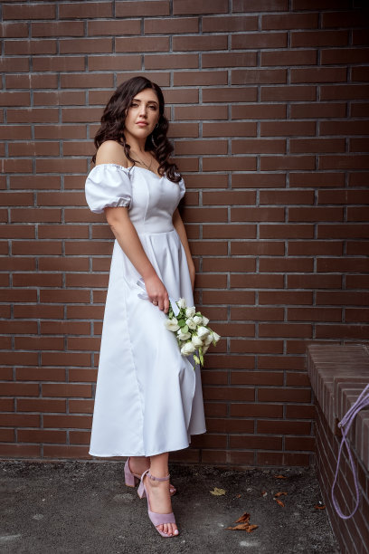 一个性感时髦的女孩，穿着白色连衣裙和粉色凉鞋，在棕色砖墙的背景下，手里拿着一束白花。复古风格的肖像。图片下载