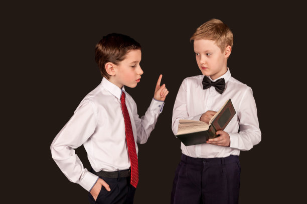 两个自信的男孩朋友，穿着白衬衫指着书，在黑色背景下孤立地交谈着。孩子们正在进行严肃的辩论。教育讨论概念。复制广告的文本空间图片下载