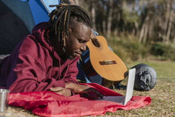 一名非裔美国男子躺在露营帐篷里使用笔记本电脑，在大自然中露营时远程工作图片下载