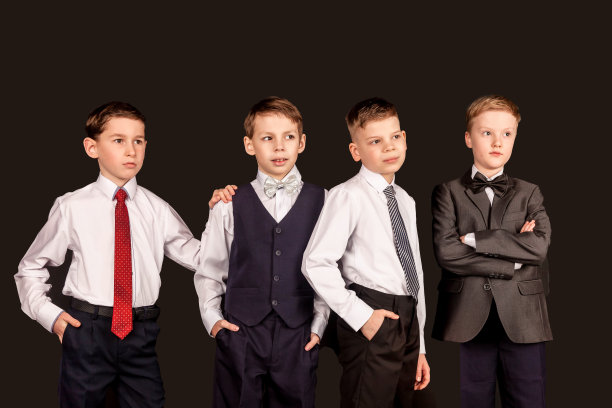 四个时髦的孩子，学龄男孩在黑色孤立的背景下摆姿势，看向别处。一群朋友，穿着时髦衣服的学生，不同种族的孩子。童年的概念。本空间图片下载