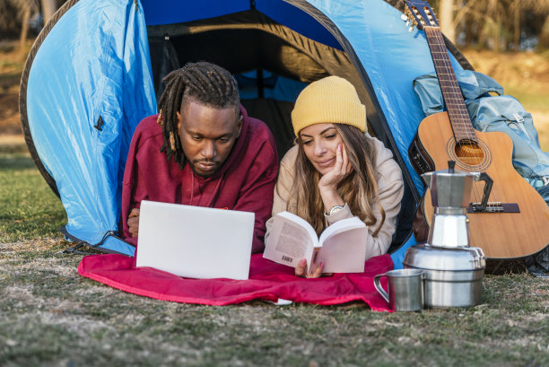 快乐的多种族夫妇躺在露营帐篷内使用小工具图片下载