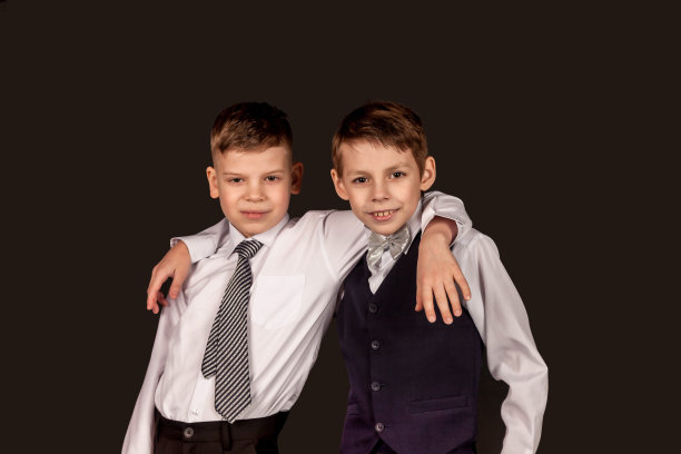 两个穿着白衬衫的快乐男孩朋友抱在一起，看着隔离在黑色背景上的相机。时髦小伙，学生，摄影棚。童年情感概念。复制广告的文本空间图片下载