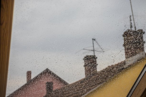 雨滴落在屋顶窗户上，映衬着房屋的背景。多雨的天气。透过水滴的窗户看到的房屋屋顶图片下载