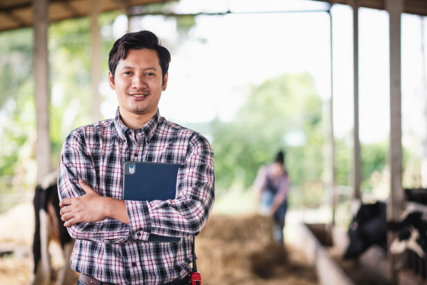 在奶牛场工作的亚洲男子手持数字平板电脑，新一代农民使用技术管理小型企业智能农场，畜牧业和农业产业。图片下载