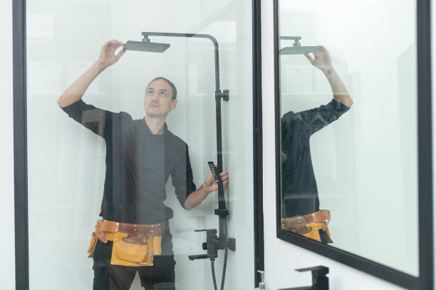 工人正在用一根金属棒连接淋浴房的玻璃墙。图片下载