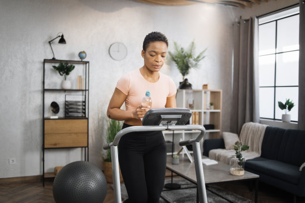 非洲妇女穿着运动服，戴着耳机，拿着一瓶水做有氧训练图片下载