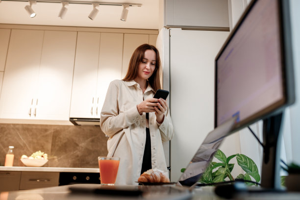 快乐的女人自由职业者在便装使用电话，而站在家里厨房在工作期间刹车图片下载