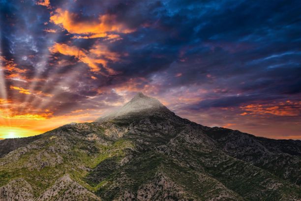 这张戏剧性的照片，太阳从一座岩石山后面发出明亮的光芒图片下载
