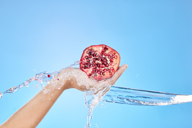 水飞溅，手和石榴为健康在工作室在蓝色背景模型。新鲜水果，清洁卫生和女模特抱着水果食物维生素c，有机化妆品或发光皮肤。图片下载