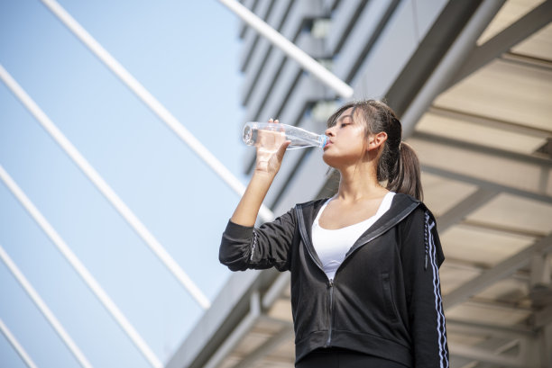 现代都市的女性在户外穿着健康运动服，喝着水瓶跑步锻炼。年轻女子在阳光明媚的户外锻炼。健康的生活方式女性概念图片下载