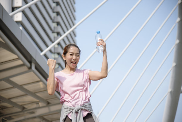 现代都市的女性在户外穿着健康运动服，喝着水瓶跑步锻炼。年轻女子在阳光明媚的户外锻炼。健康的生活方式女性概念图片下载