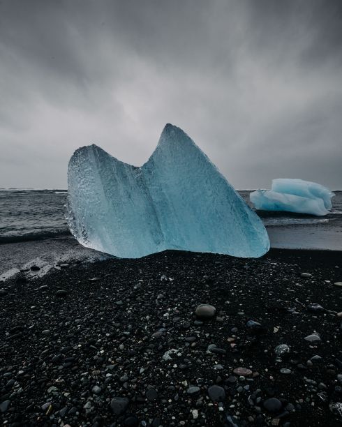 在一个阴沉的日子里，冰山在卵石海滩上对着海浪的垂直拍摄图片下载