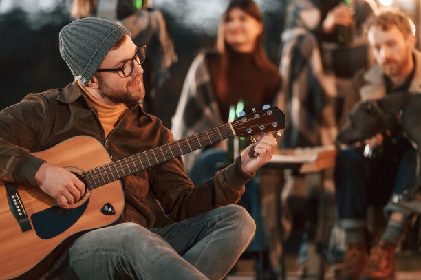 戴帽子的人正坐着弹吉他。晚上一群人在后院一起玩图片下载