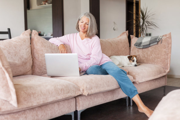 成熟女子坐在沙发上使用无线笔记本电脑应用程序浏览互联网图片下载