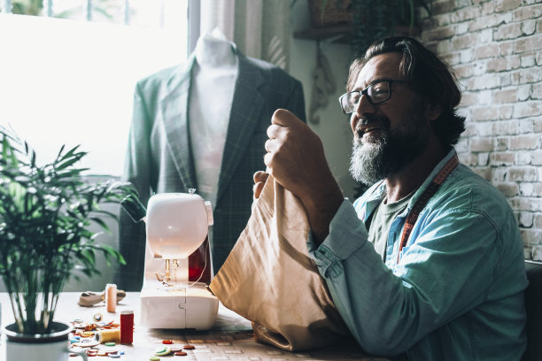 快乐的工人在车间。裁缝独自使用缝纫机，微笑着工作。另一种手工工作。成年男性在为时尚生意做裁缝。专业人士画像图片下载