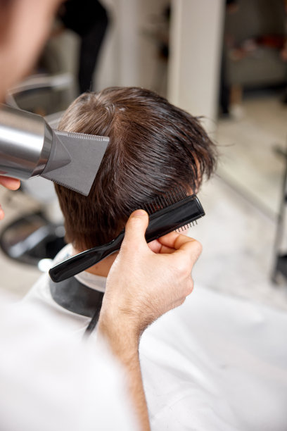 专业发型师在理发店为男性客户工作时使用吹风机。在理发店理发。图片下载