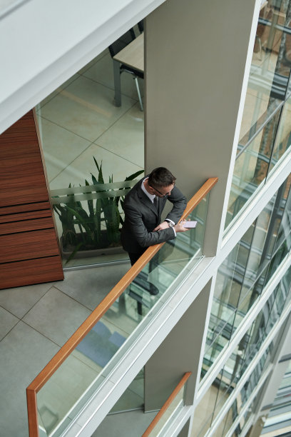 穿着西装的年轻男性员工站在办公中心的栏杆边发短信图片下载