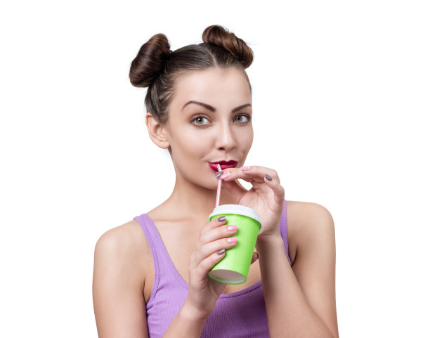 年轻漂亮的女孩用吸管从白色背景的纸杯中喝水。图片下载