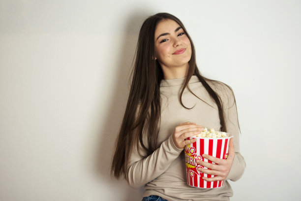年轻漂亮的女人在灰色的墙外吃爆米花图片下载