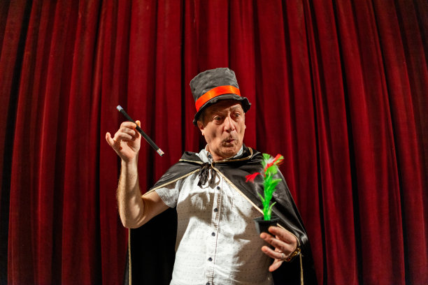 白人男魔术师在剧院舞台上用魔杖和假花表演魔术图片下载