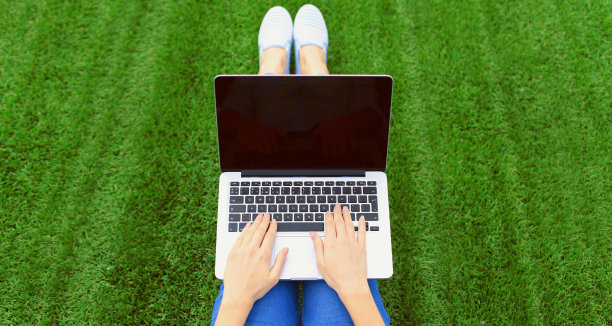 女子手握笔记本电脑工作，在公园绿草背景下的空白黑屏图片下载