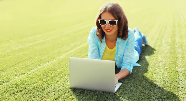 年轻女子与笔记本电脑在公园绿草背景图片下载