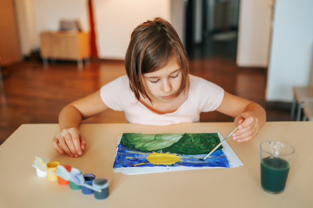 一个可爱的女孩坐在桌前用毛笔画画，目不转睛地看着画，迷离了。图片下载