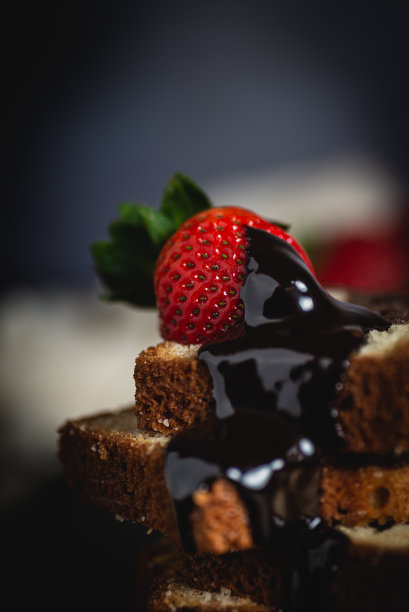 前景是一颗有机草莓，蘸着液体巧克力倒在海绵蛋糕上，背景是草莓图片下载