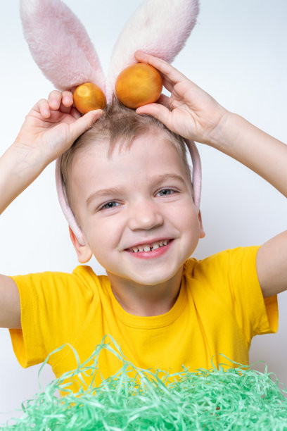 孩子们庆祝复活节。一个戴着兔子耳朵的有趣的孩子正在模仿草的绿色纸上寻找复活节彩蛋图片下载