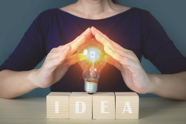 女企业家手持发光的灯泡，在写有IDEA字样的木块上输入商业战略理念、创造性思维理念和创新理念。图片下载