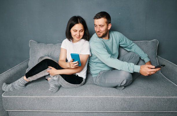 年轻夫妇在家里用智能手机在沙发上放松图片下载