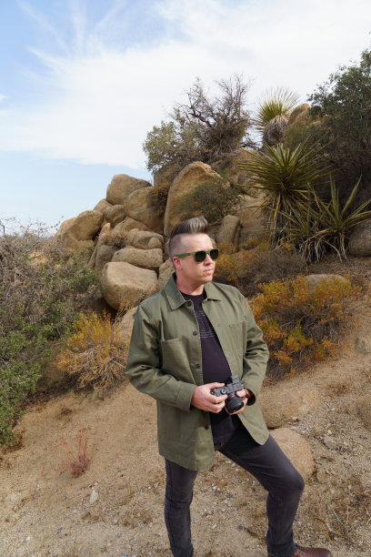 在约书亚树街，一名戴墨镜、身穿黑色外套、身穿绿色夹克的男子拿着相机图片下载